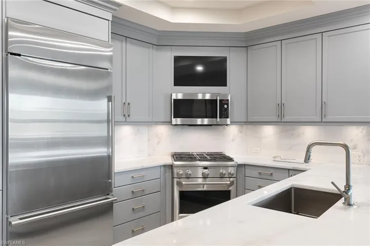 Kitchen with high quality appliances, gray cabinetry, light stone countertops, and decorative backsplash