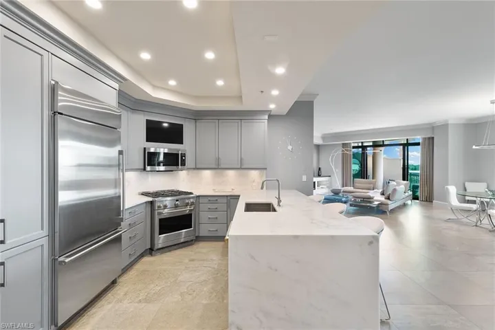 Kitchen with gray cabinets, light stone countertops, a peninsula, a breakfast bar area, and premium appliances