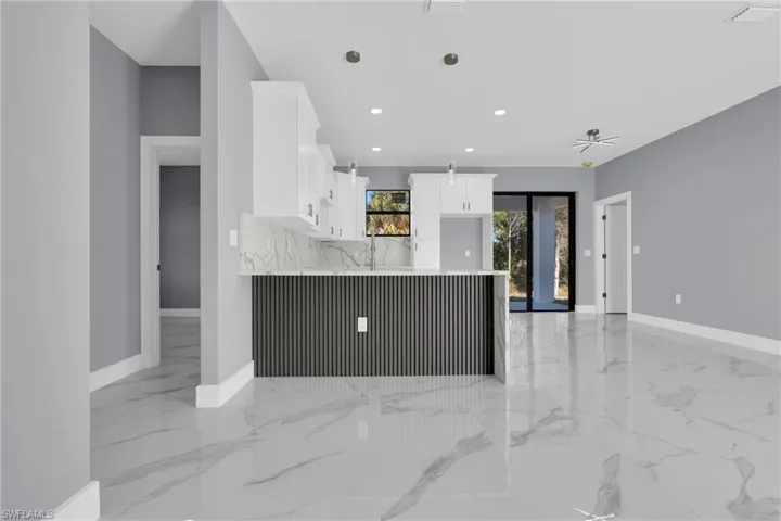 Kitchen featuring white cabinetry, light stone counters, pendant lighting, a peninsula, and light marble finish flooring