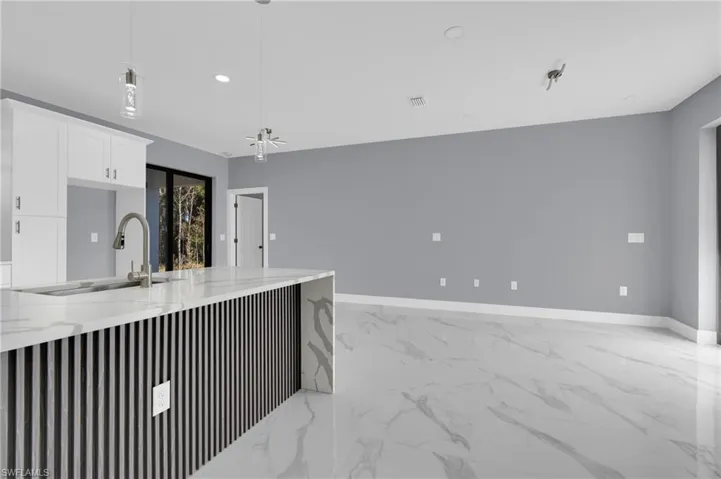 Kitchen with light marble finish floors, light stone counters, white cabinets, decorative light fixtures, and a ceiling fan