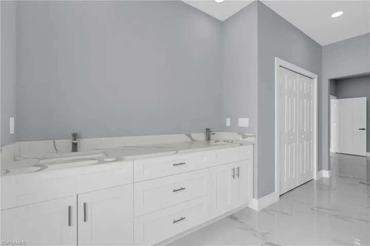 Full bath with double vanity, light marble finish floors, and recessed lighting