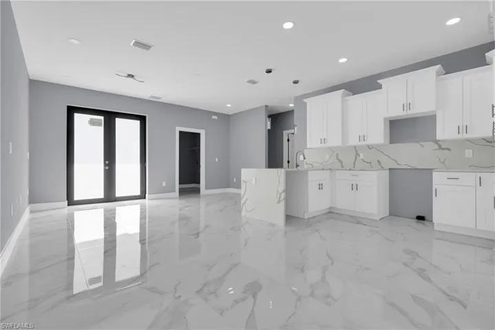 Kitchen featuring light stone counters, white cabinets, french doors, recessed lighting, and backsplash