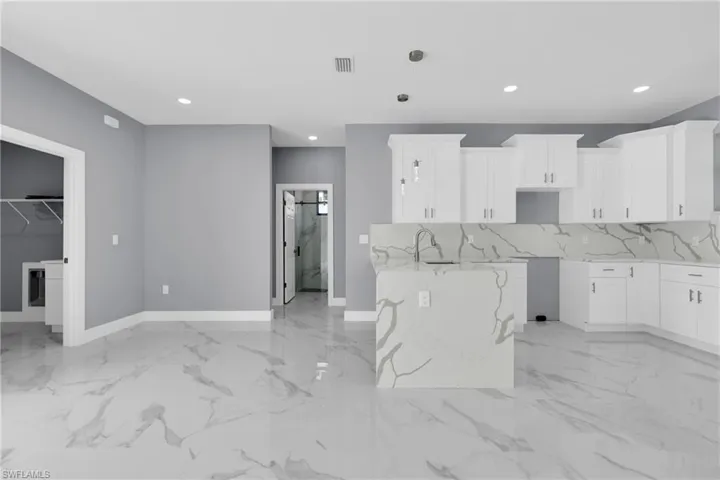 Kitchen featuring light stone countertops, white cabinetry, hanging light fixtures, and backsplash