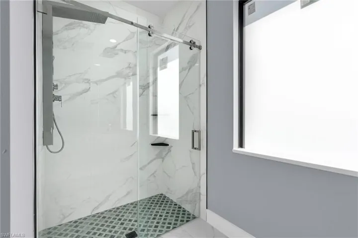 Bathroom with a marble finish shower and baseboards