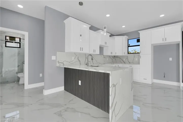 Kitchen featuring light stone countertops, white cabinetry, a peninsula, light marble finish flooring, and hanging light fixtures