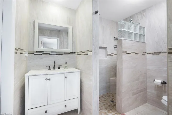Bathroom featuring vanity, walk in shower, and tile walls