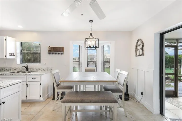Dining space featuring a ceiling fan, a wainscoted wall, light tile patterned floors, a decorative wall, and a chandelier