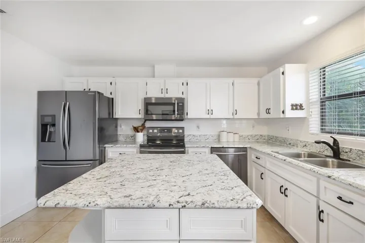 Kitchen with white cabinetry, stainless steel appliances, a kitchen island, light stone counters, and light tile patterned floors
