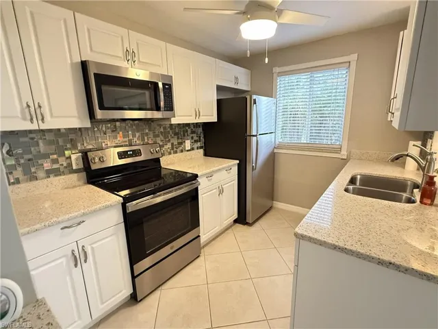Kitchen with stainless steel appliances, white cabinetry, light stone countertops, light tile patterned floors, and ceiling fan