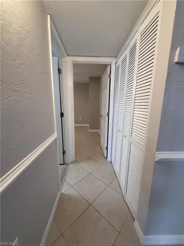 Corridor with a textured wall and light tile patterned floors that leads to common bathroom and 2nd bedroom
