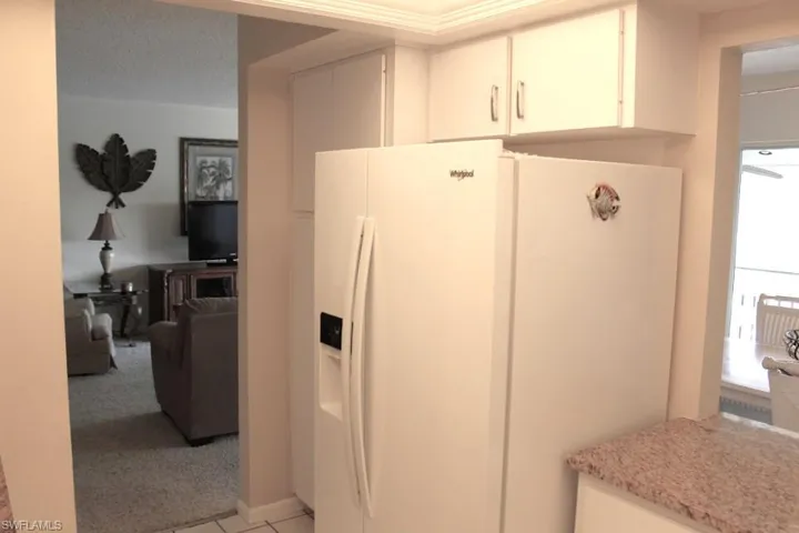 Kitchen featuring white refrigerator with ice dispenser, white cabinetry, light carpet, and light stone countertops