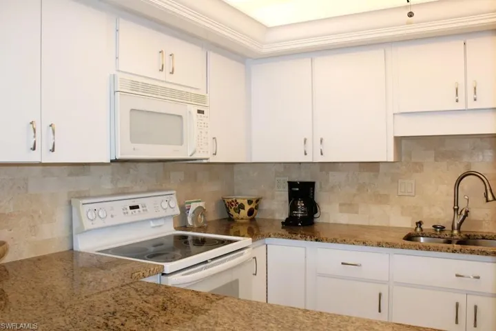 Kitchen with white appliances, white cabinetry, and decorative backsplash
