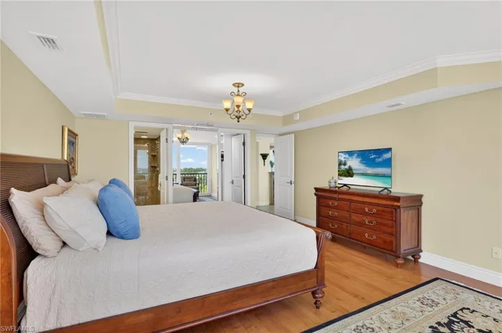 Bedroom featuring a raised ceiling, wood finished floors, a chandelier, and crown molding