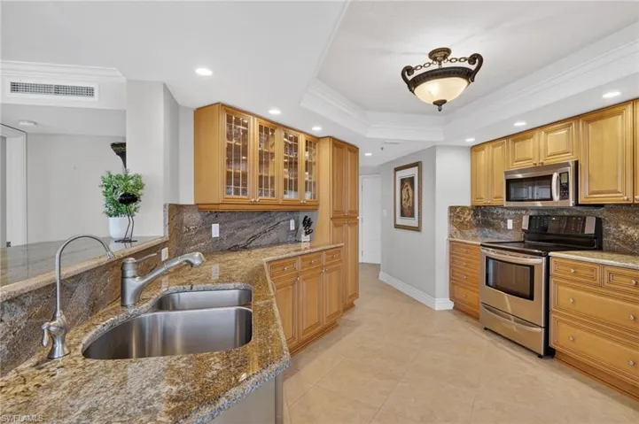 Kitchen featuring stainless steel appliances, ornamental molding, light stone countertops, recessed lighting, and glass insert cabinets