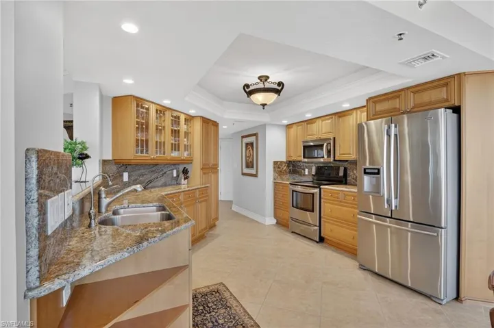 Kitchen featuring light stone counters, stainless steel appliances, recessed lighting, glass insert cabinets, and ornamental molding