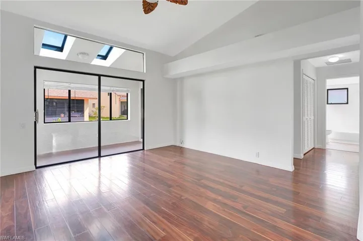 Empty room featuring dark wood-type flooring, vaulted ceiling with skylight, and ceiling fan