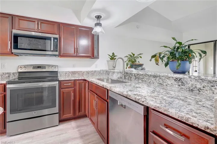 Kitchen with appliances with stainless steel finishes, light stone counters, decorative light fixtures, and sink