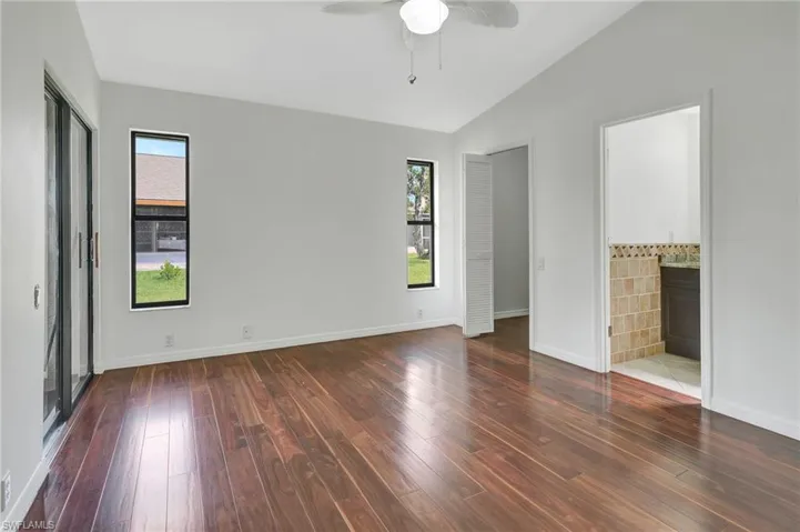 Unfurnished bedroom with dark wood-type flooring, ceiling fan, ensuite bathroom, and vaulted ceiling