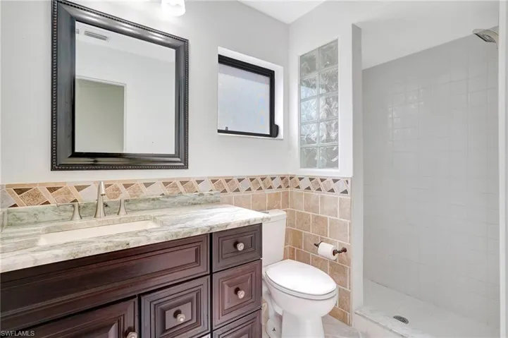 Bathroom with tile walls, toilet, a tile shower, and vanity