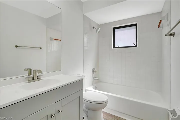 Full bathroom featuring hardwood / wood-style floors, tiled shower / bath, toilet, and vanity