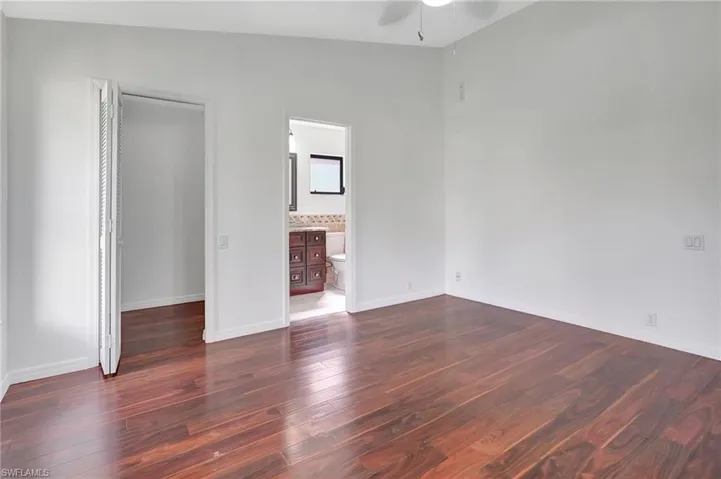 Unfurnished bedroom with dark wood-type flooring, ensuite bath, ceiling fan, and vaulted ceiling