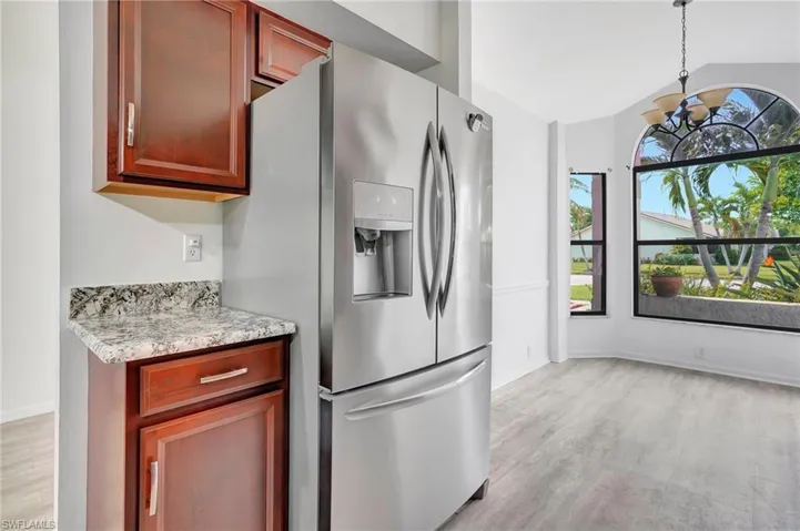 Kitchen featuring vaulted ceiling, light wood-type flooring, light stone counters, stainless steel refrigerator with ice dispenser, and pendant lighting