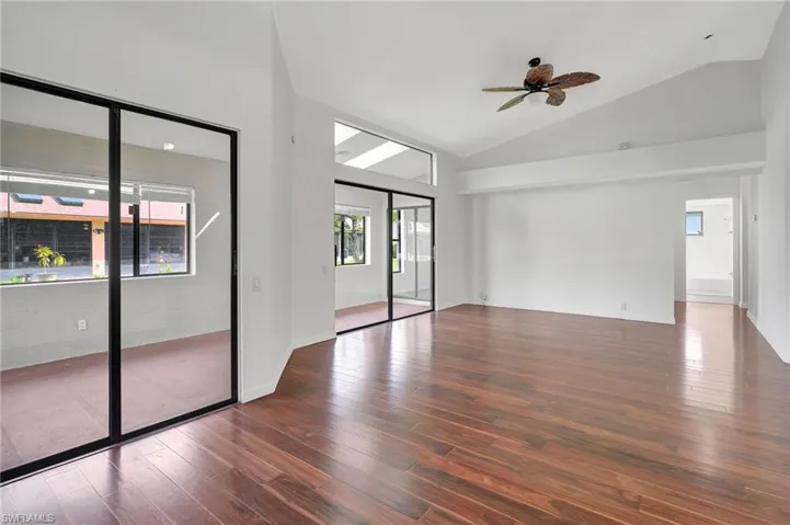 Empty room featuring dark wood-type flooring, ceiling fan, a wealth of natural light, and high vaulted ceiling