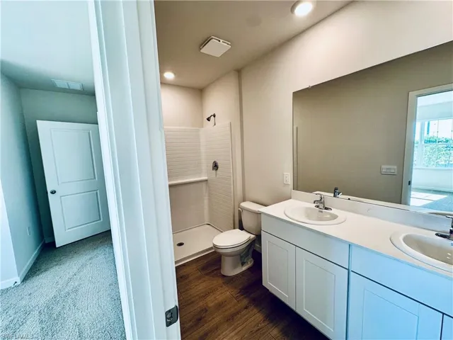 Full bathroom with double vanity, a stall shower, and dark wood-type flooring