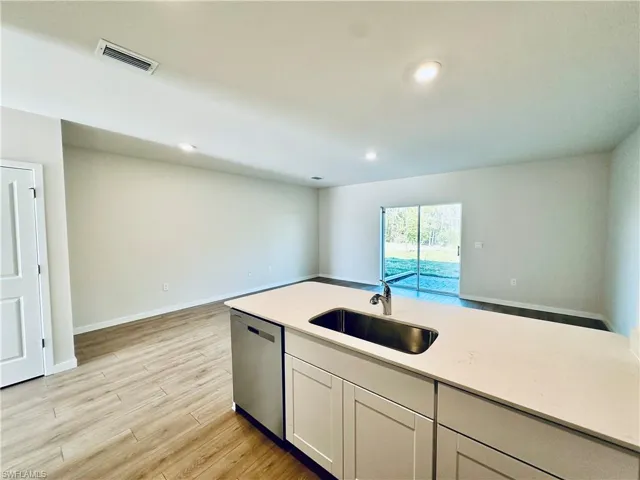 Kitchen with stainless steel dishwasher, light wood-style flooring, open floor plan, white cabinets, and light stone counters