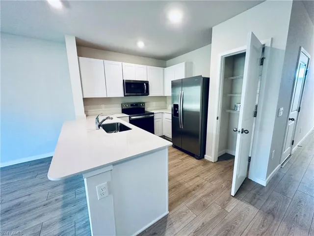Kitchen featuring a peninsula, appliances with stainless steel finishes, white cabinetry, a kitchen breakfast bar, and light stone countertops
