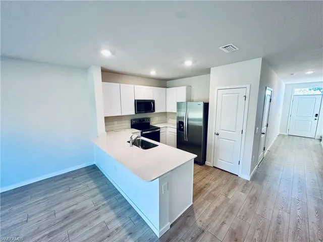 Kitchen with white cabinetry, a peninsula, stainless steel fridge, range with electric cooktop, and black microwave