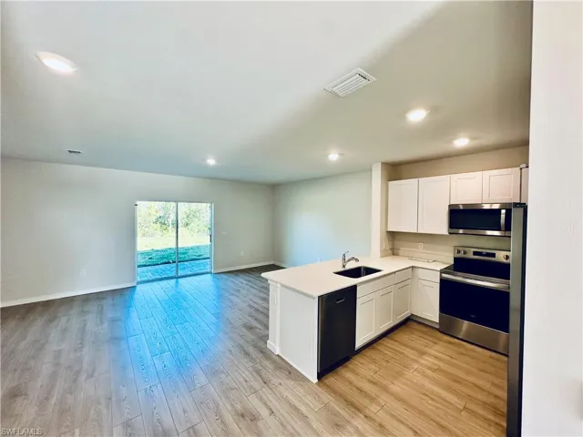 Kitchen with stainless steel appliances, white cabinetry, a peninsula, light wood-type flooring, and recessed lighting