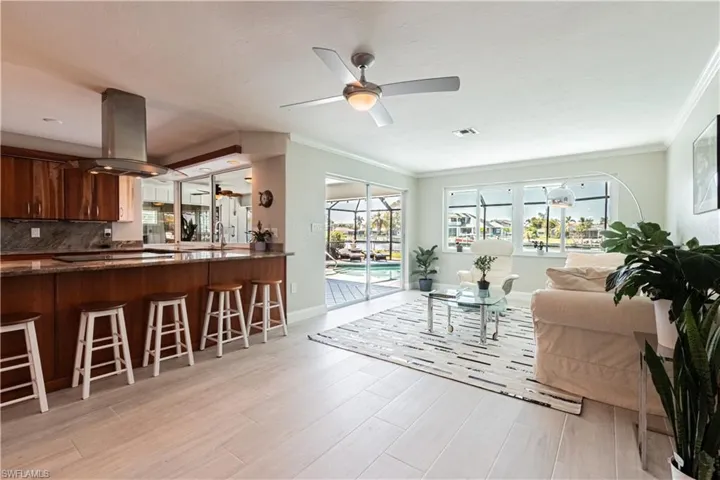 Living area with a ceiling fan, ornamental molding, healthy amount of natural light, and light wood-style floors