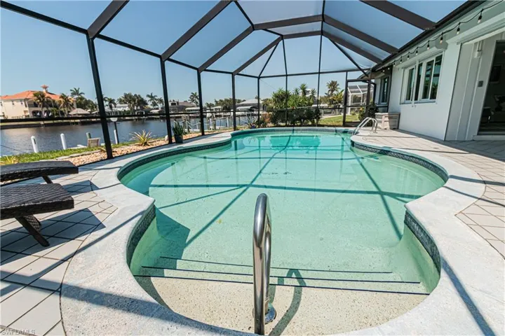 Outdoor pool featuring a patio, a sunroom, glass enclosure, and a water view