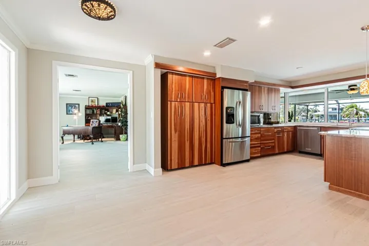 Kitchen with an office area, brown cabinets, stainless steel appliances, light wood-type flooring, and decorative light fixtures