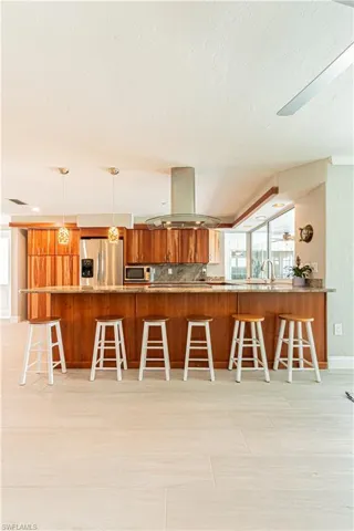 Kitchen with brown cabinets, a kitchen breakfast bar, appliances with stainless steel finishes, island range hood, and a textured ceiling