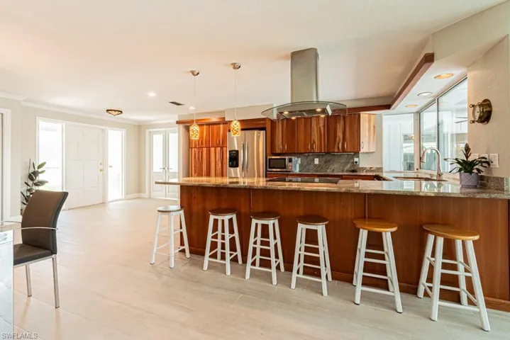 Kitchen with a peninsula, a breakfast bar area, dark stone counters, backsplash, and island range hood