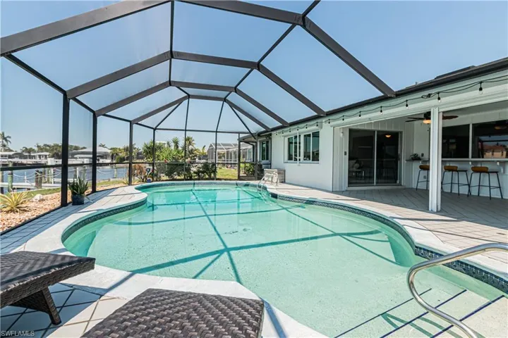 Swimming pool with glass enclosure, a patio area, a sunroom, a ceiling fan, and a water view
