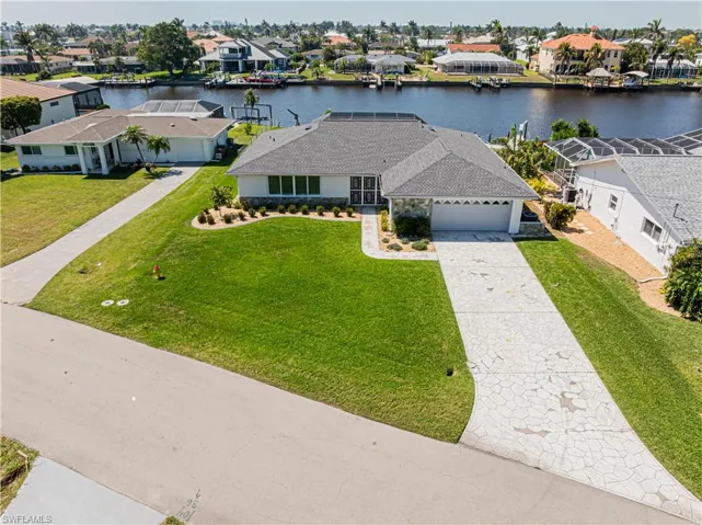 View of front of property with a water view, a residential view, concrete driveway, a garage, and a front lawn