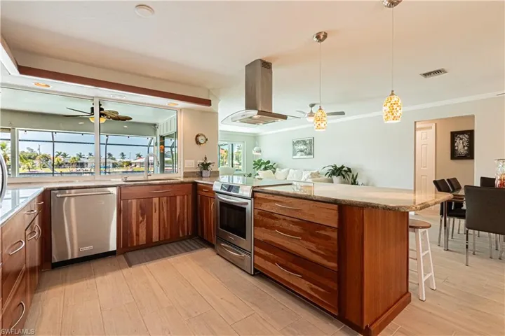 Kitchen with ceiling fan, light stone counters, brown cabinetry, appliances with stainless steel finishes, and island range hood