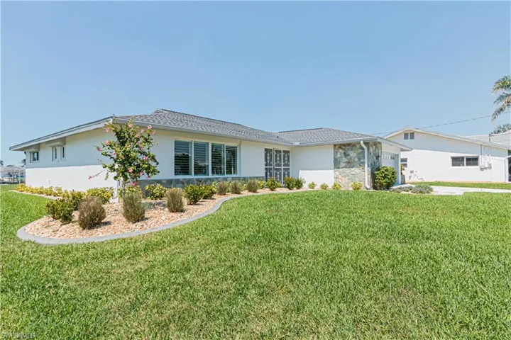 Back of property with a yard, stone siding, a garage, and stucco siding