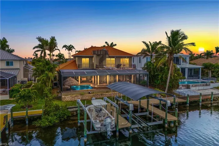 Back house at dusk featuring a lanai, a patio area, a water view, and a balcony