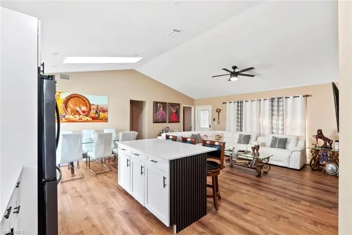 Vaulted ceiling with skylight, wood-finish flooring, white kitchen island with countertop, and black ceiling fan