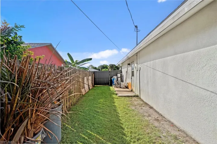 Expansive side yard featuring a manicured lawn, wood picket fencing, and a concrete patio