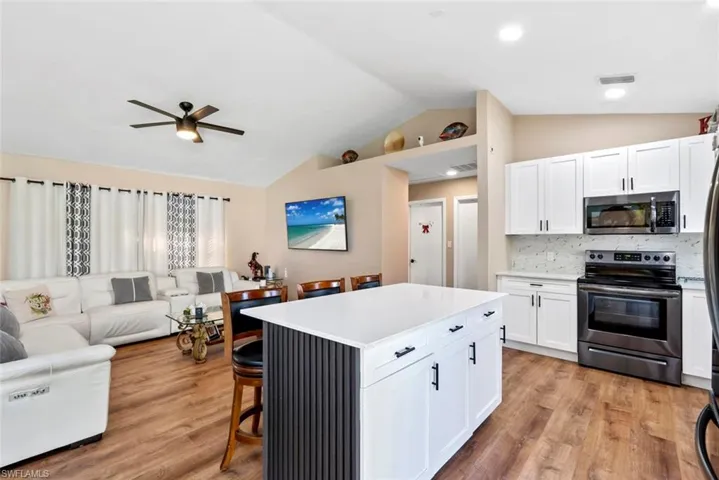 Kitchen island with a white countertop and dark gray slatted paneling, white cabinetry with dark hardware, stainless steel appliances, and wood-finish flooring