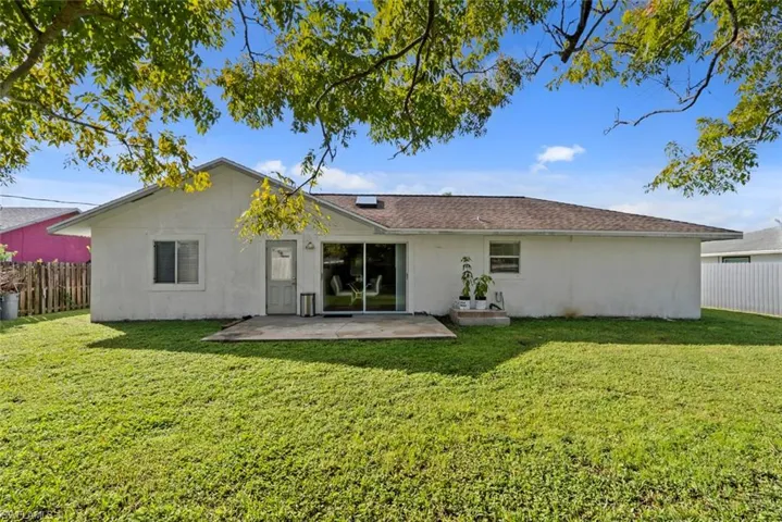Expansive rear yard featuring a concrete patio, sliding glass doors, and a partial wood fence