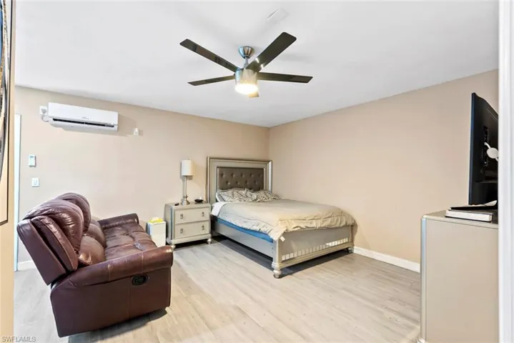 Light-tone wood-finish flooring, ceiling fan with integrated lighting, wall-mounted air conditioning unit, and neutral wall tones