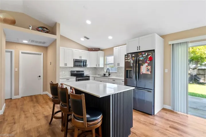 Kitchen featuring wood-finish flooring, vaulted ceilings, white shaker cabinetry, a central island with a white countertop, and a sliding glass door to the exterior