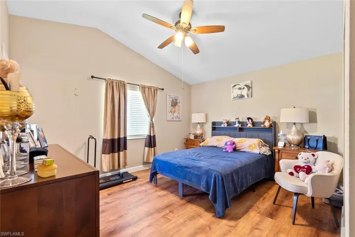 Vaulted ceiling with a ceiling fan, wood-finish flooring, and a window with blinds