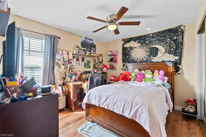 Wood-finish flooring, ceiling fan with integrated lighting, window with blinds, recessed wall shelving